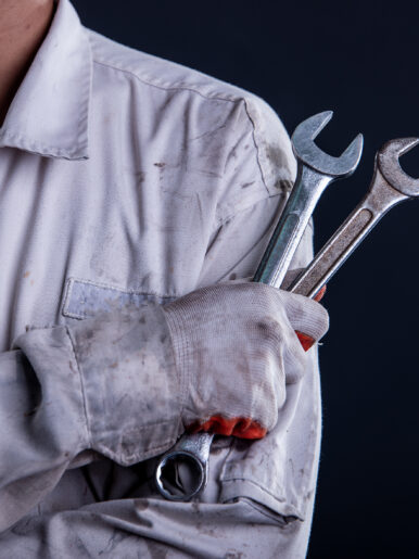 Car mechanic wearing a white uniform stand holding wrench isolated on gray background with copy space.