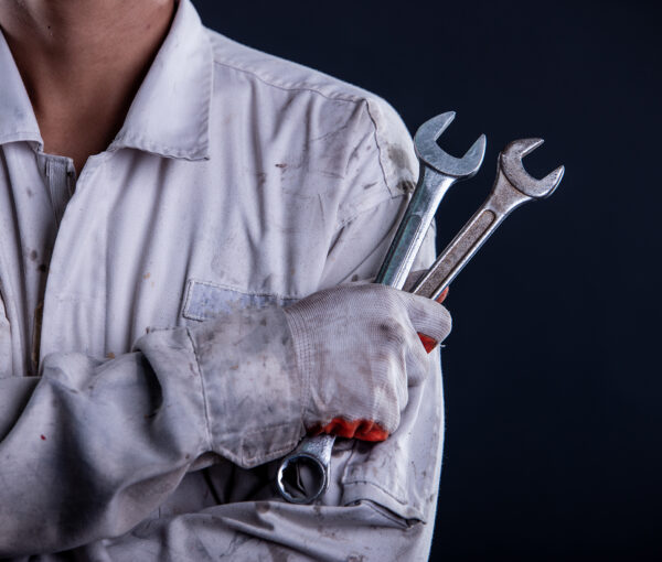 Car mechanic wearing a white uniform stand holding wrench isolated on gray background with copy space.